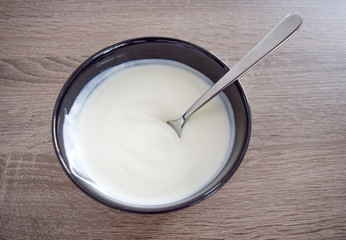 Bowl of white yogurt with spoon isolated on vintage rustic wooden table from above, plain yoghurt