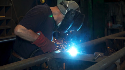 Worker with protective mask welding metal. A man welds a metal with a welding machine. Welder is...