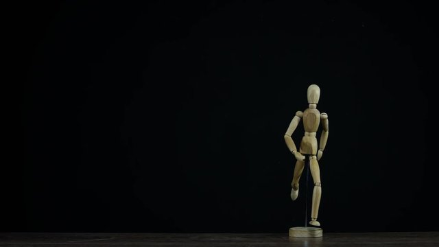 Stopmotion running wooden figure dummy rotates in studio on black background for titles