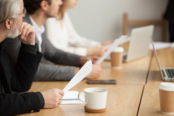 Attentive senior businessman holding documents focused on listening at group meeting, aged...