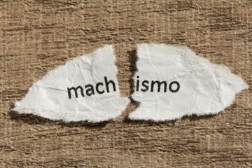 Torn paper written machismo, portuguese and spanish word for chauvism, over wood table. Concept of old and abandoned idea or practice. - obrazy, fototapety, plakaty