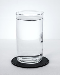 Black beverage coasters with water glass on white background. Pure water in transparent glass.