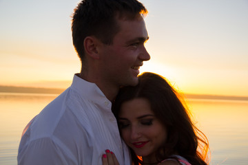 Young couple is embracing in the water on summer beach. Sunset over the sea.Two silhouettes against the sun. Just married couple hugging. Romantic love story. Man and woman in holiday honeymoon trip.