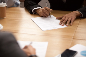 Businessman in suit signing business contract at meeting, entrepreneur putting written signature filling legal document at negotiations, two partners making partnership deal concept, close up view