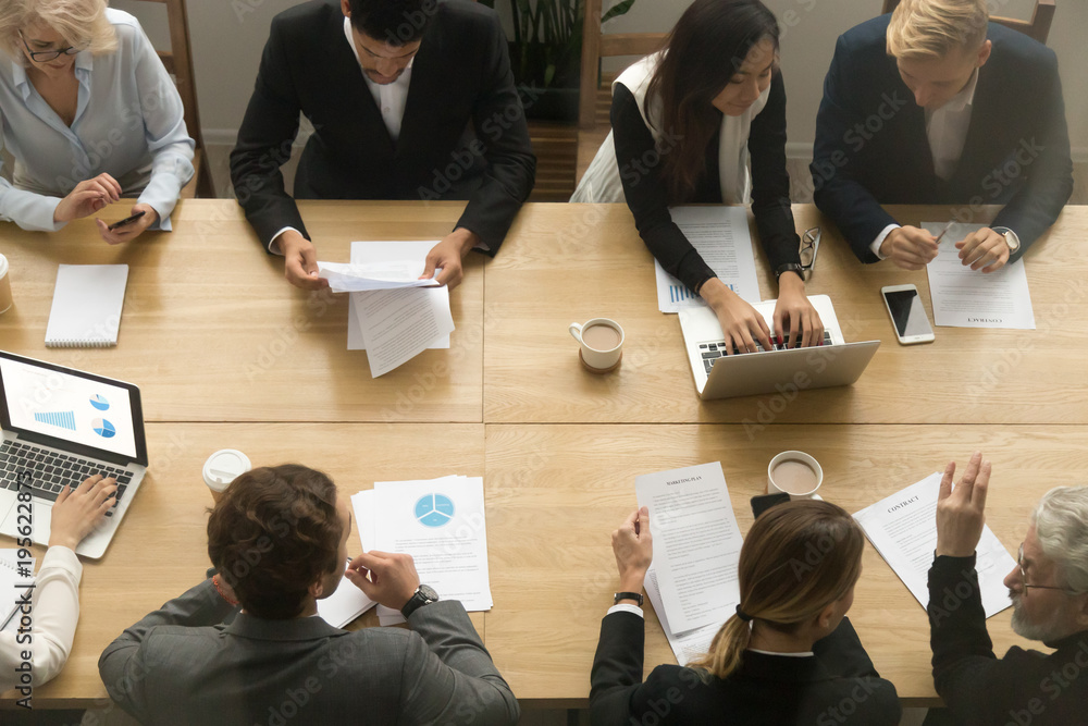 Poster diverse senior and young business people sitting at conference table working together using devices 