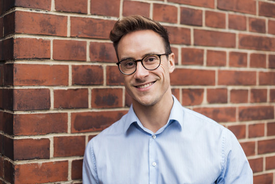 Portrait of smiling young businessman at brick wall