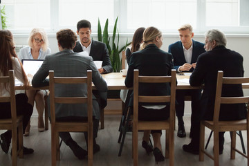 Serious multi-ethnic business people team sitting at conference table, senior executives working together with young managers at office staff meeting, focused group negotiations or teamwork concept