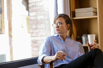 Young woman with coffee cup looking out of office window