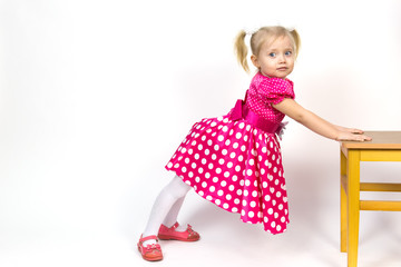 A beautiful young blond girl leans her elbows on a chair and puts her head on her hands. Little girl 3 years old on a white background put her head on her hands.
