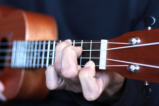 left musician hand clamps the chord on the ukulele fretboard