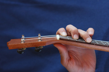 left musician hand clamps the chord on the ukulele, top view