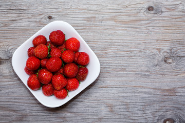 Strawberries berries on a white plate on a wooden table. Copy text. Close up.
