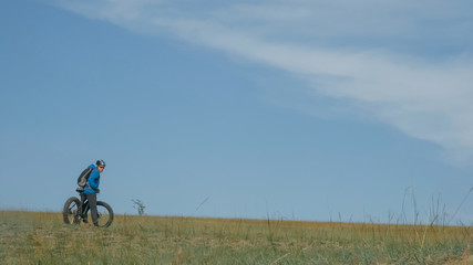 Fat bike also called fatbike or fat-tire bike in summer driving through the hills. The guy is riding a bike along the sand and grass high in the mountains. He performs some tricks and runs dangerously