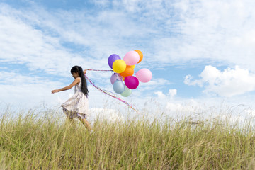 Happy woman jumping with air balloons on the meadow.