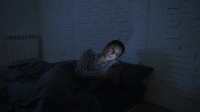low light video lateral panning shot of young attractive hispanic woman 30s in bed late night using mobile phone looking tired bored in internet communication addiction concept 