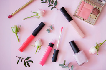 Lip gloss, nail polish, pencil, blush with flowers on a pink background