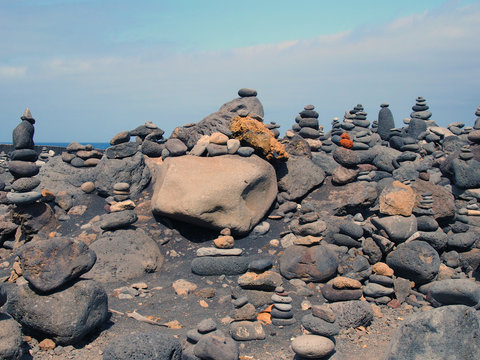 towers of stacked pebbles and stones in different colours in a large arrangement on a black sand beach with blue sky