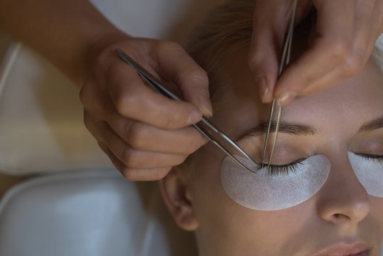 Aesthetician giving eyelash extension treatment to customer's eyes