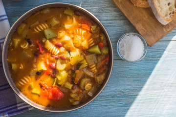 Traditional minestrone soup with pasta in a plate on a rustic wooden table, sunny day  - copy space for a recipe