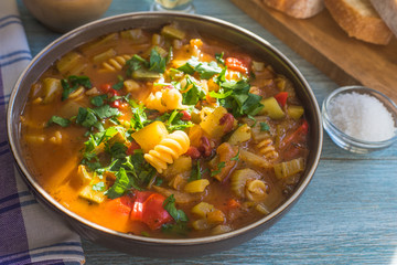 Traditional minestrone soup with pasta in a plate on a rustic wooden table close-up, sunny day - top view