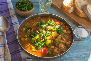 Traditional minestrone soup with pasta in a plate on a rustic wooden table close-up, sunny day - top view