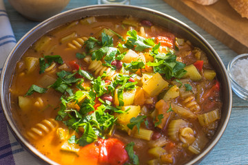 Traditional minestrone soup with pasta in a plate on a rustic wooden table close-up, sunny day - top view