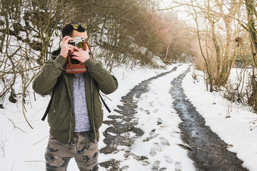 Hipster bearded man with retro camera standing in mountains forest background in winter day