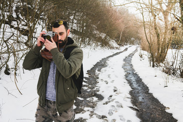 Hipster bearded man with retro camera standing in mountains forest background in winter day