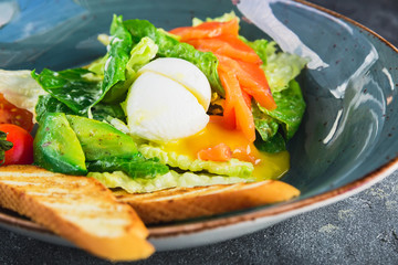 Caesar salad with egg, salmon, avocado, cherry tomatoes and grilled bread. Close up view