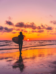 Silhouette of the surfer girl with surfboard on a beach at sunset. Surfer and ocean
