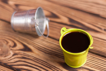 Full green bucket of black coffee near empty zinked metal bucket with handle on old worn wooden table