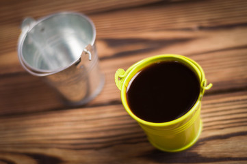 Full green bucket of black coffee near empty zinked metal bucket with handle on old worn wooden table
