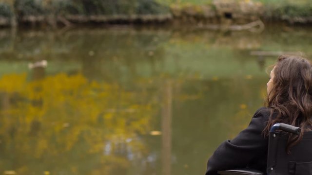 sad and depressed woman on wheelchair contemplates the lake