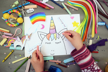 The child draws the unicorn's face with colored pencils on a gray background