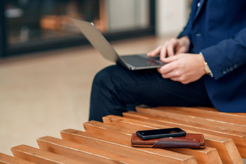 A businesswoman working on a laptop sitting on a bench, close up. Forex cryptocurrency trading, business concept. Leather wallet and smartphone on the branch. Selective focus.