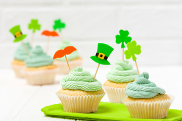 St. Patrick's Day theme colorful horizontal banner. Cupcakes decorated with green buttercream and craft felt decorations in form of leprechaun hat, mustache, shamrock leaves on white background