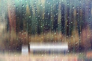 glass wet autumn background, rain in the park glass wet surface with reflection, rain drops on the drenched window glass, background window in the autumn park, autumnal rainy landscape blurred