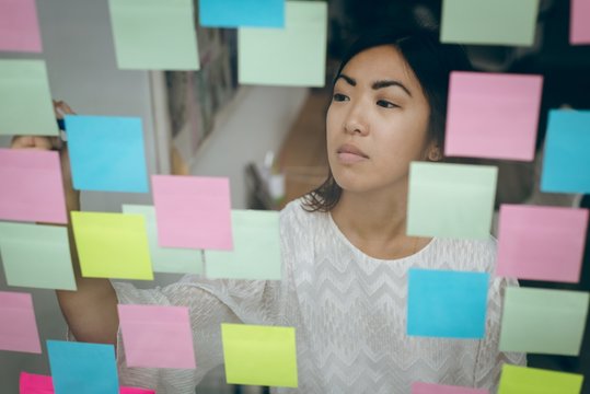 Female executive sticking adhesive notes on glass wall