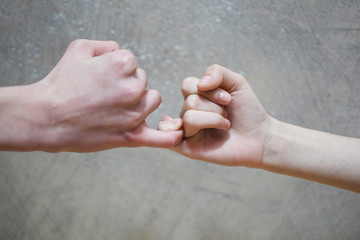 Pinky swear handshake of teenage brother and sister on blur grey brown wall background.