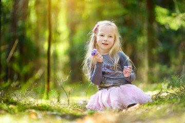 Adorable little girl picking the first flowers of spring in the woods on beautiful sunny spring day