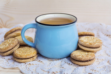 blue mug of tea and sandwich cookies on wooden background 