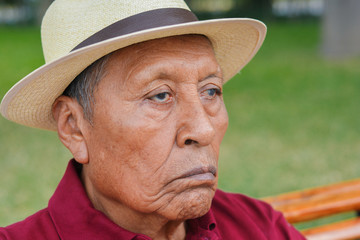 Sad old latin man wearing hat in the summer park.