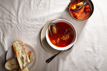 Traditional mediterranean soup bouillabaisse with mussels, shrimps, tomatoes and fish broth served in copper saucepan and white bowl with warm baguette and cheese. Holiday meal concept