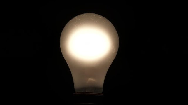 Close up on incandescent light bulb turning on and off with a little flicker.