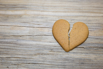 Broken heart shaped gingerbread on wooden background.