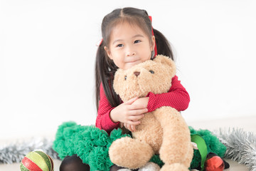 Happy Cute Asian Girl in Red and Green Colour is hugging a Teddy Bear in White room Background. Happy thanksgiving and Party Concept.