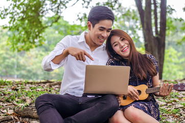 Young couple relaxing in the garden she playing a ukulele and he reading on notebook. Lifestyle in relax time and holiday