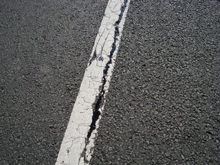 White single dividing line over highway asphalt with a crack