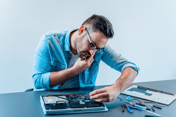 Handsome computer engineer talking on a mobile phone while repairing laptop computer.