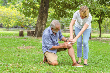 Old man with pain on his knee and woman gives him first aid